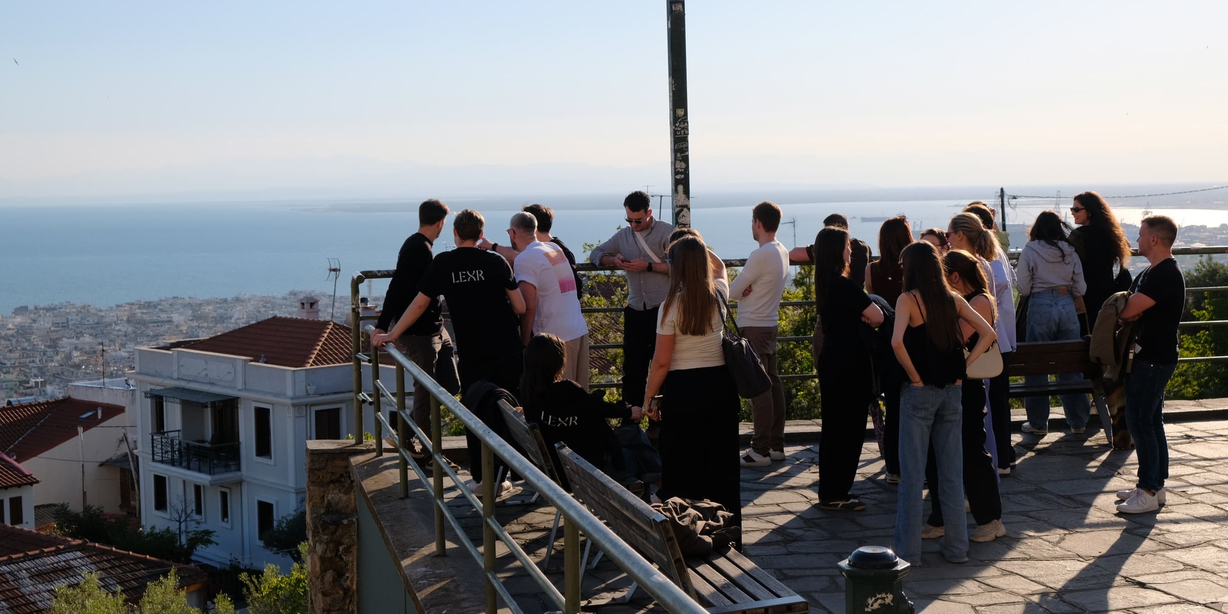 The LEXR team at a railing on a terrace above Thessaloniki, looking out over the bay and the city roofs in late afternoon light