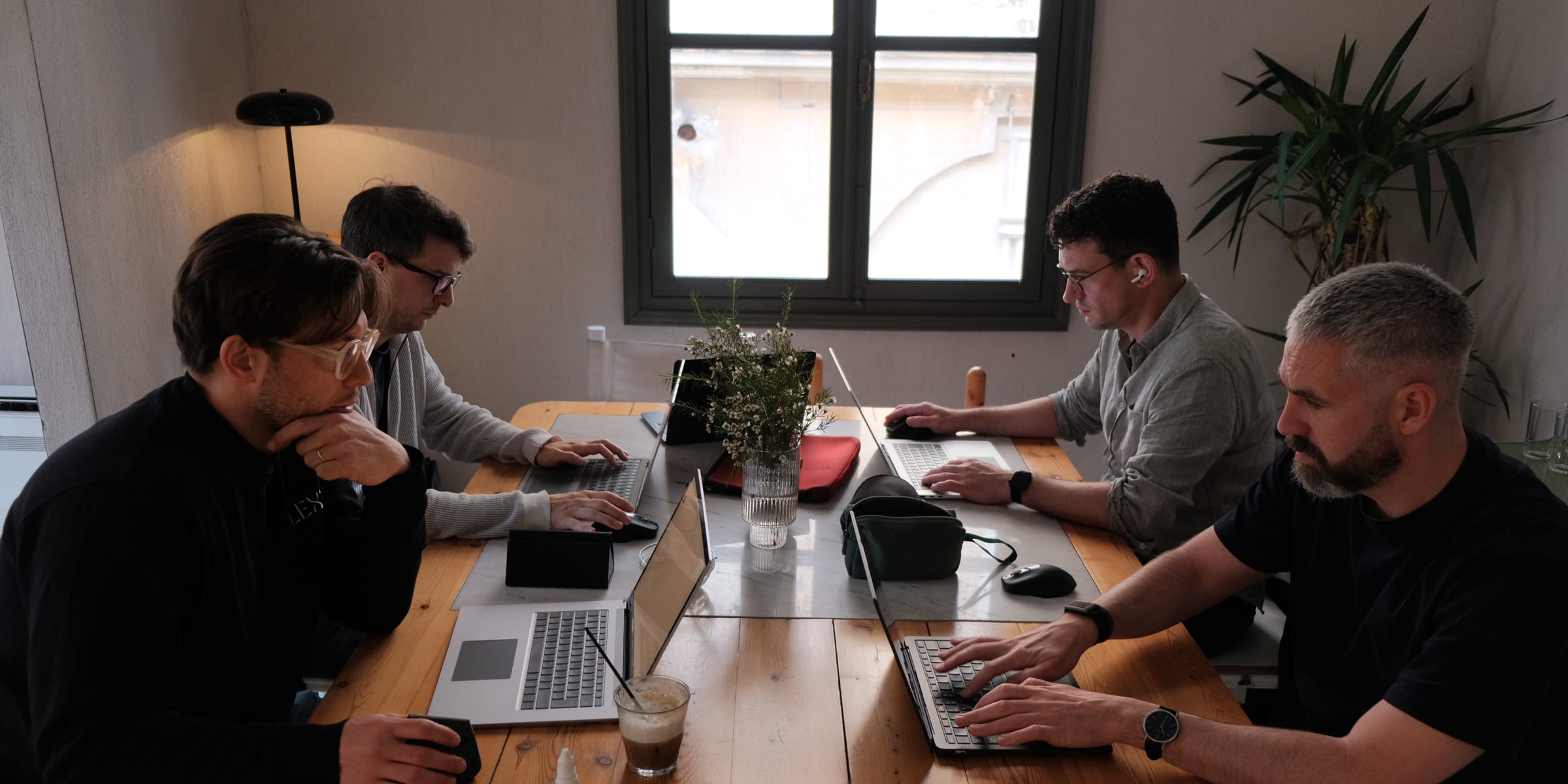 Four LEXR lawyers working on laptops along a long wooden table, a window and a plant behind them